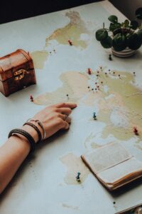 Mapa del mundo con puntos señalados, una mano que señala un lugar y un libro abierto sobre el mapa