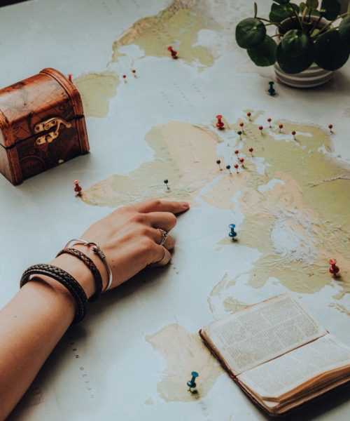 Mapa del mundo con puntos señalados, una mano que señala un lugar y un libro abierto sobre el mapa